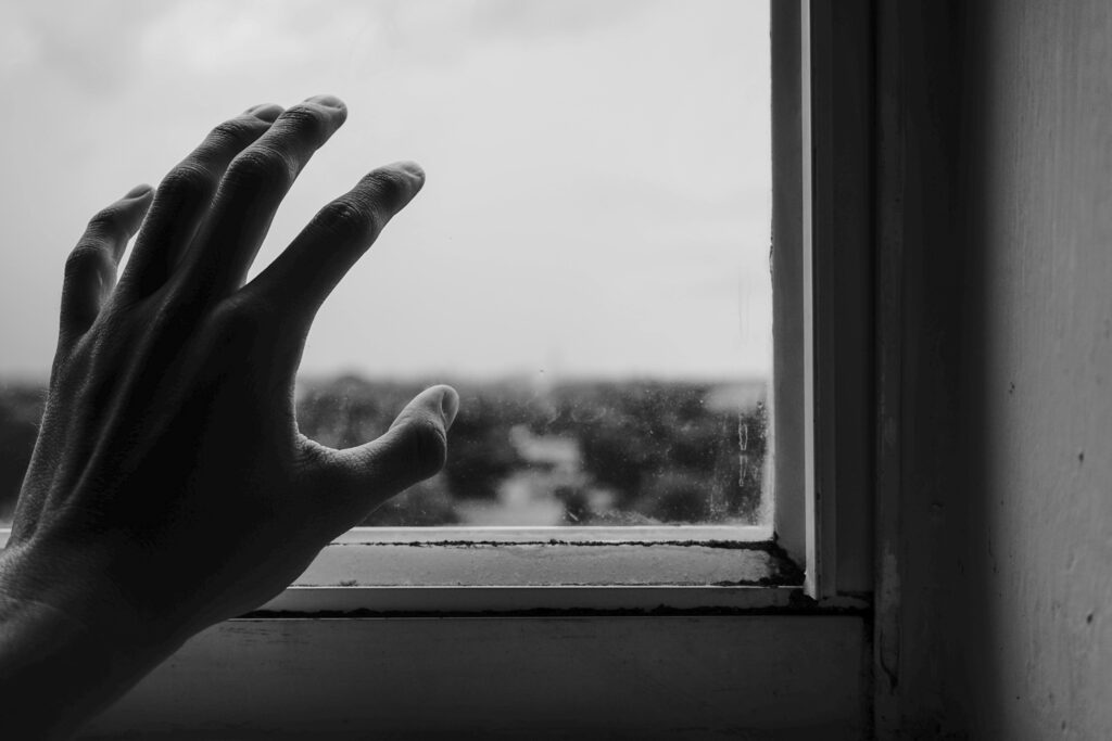 Abstract monochrome photo of a hand reaching towards a window, symbolizing longing.